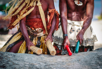 Two native Fijian men in traditional dress beating log ithe sticks making music