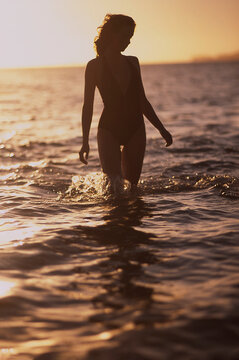 Young woman walking in water and sun setting in background in tropical Fiji
