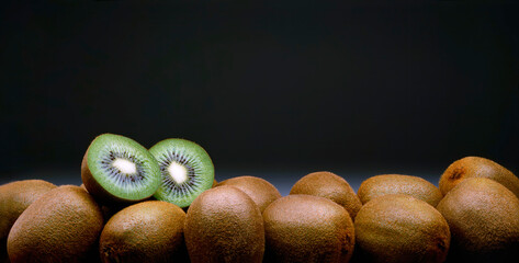 Panorama of kiwifruit on black background with one cut in half