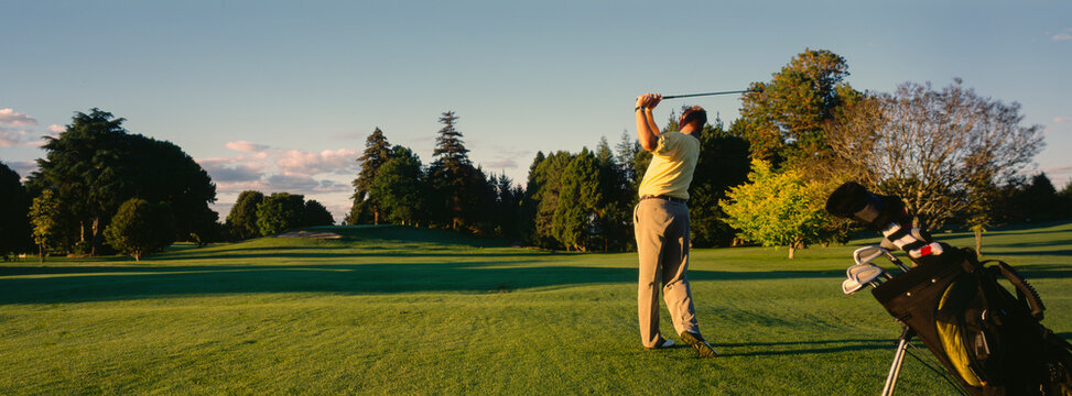 Panorama of man swinging golf club on pristine golf course