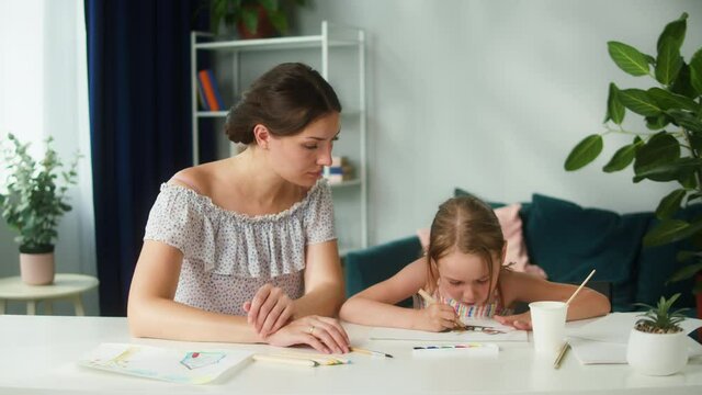 Young mother teaching her daughter to draw. Lovely babysitter drawing with little girl at home. Motherhood and happy childhood concept. Preschool children education.