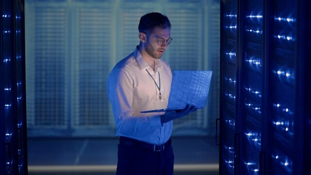 Male Server Engineer in Data Center. IT engineer inspecting a secure server cabinet using modern technology laptop coworking in data center.