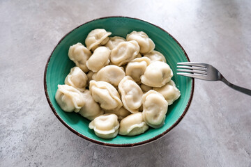 Tasty meat dumplings in green plate with fork on a table, russian pelmeni