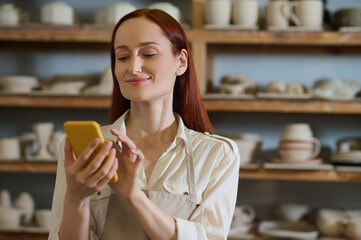 Young pretty woman with a smartphone in a pottery workshop