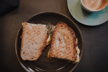 Flat lay view of a half full cup of coffee and toasted cheese bread on a brown table