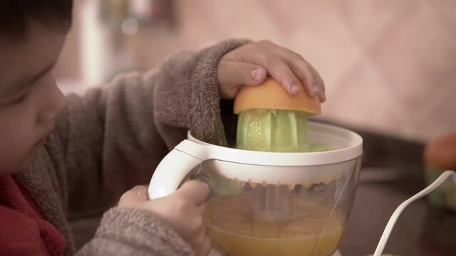 Slow motion close up footage of a kid learning to make fresh orange juice. Using electric squeezer for fruit.