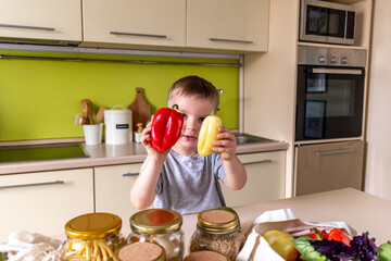 Boy standing in the kitchen and sorting out groceries from the store. Sweet pepper in the hands of a child.