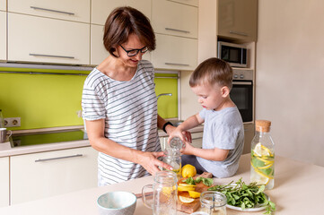 Obraz na płótnie Canvas Adult woman is preparing lemonade with her son. Cold drink. Summer heat. Vegetarian food concept.