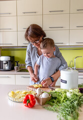 Boy child helps his mom to cook vegetable ratatouille standing in the kitchen. Family traditions.