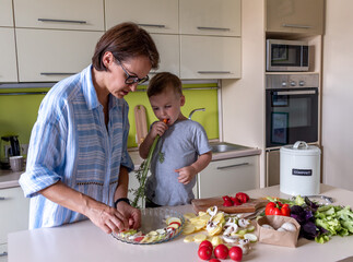 Boy child helps his mom to cook vegetable ratatouille standing in the kitchen. Family traditions.