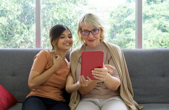 Asian daughter take a selfie with her adopted caucasian mother through a tablet computer. Happy mix skin family living together.