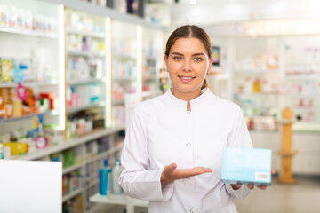 Female pharmacist standing in drugstore and holding drug package in hands