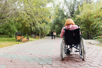 Young disabled woman in wheelchair in park looking at couple of people leaving.  Sadness and...