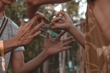 Closeup of two people playing the Cat's cradle with a thread outdoors