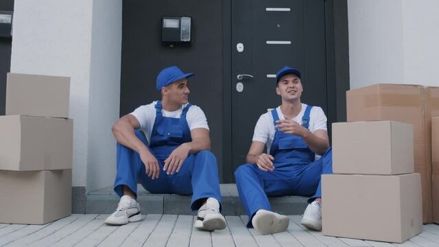 Two removal company workers have a break while sitting on the step