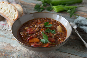 a bowl of lentil soup with chorizo on a wooden table