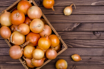 Large raw onions in a box on a wooden background.