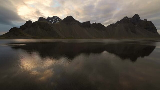 Vestrahorn mountain reflections in calm water and cloudy evening sky with rays of the sun
