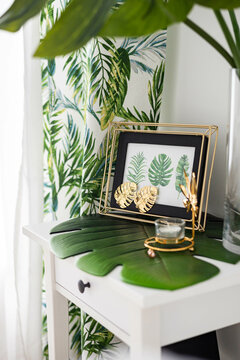 Cozy domestic interior decor with tropical green leaves, copper photo frame luxury home design