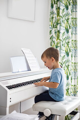 Cute baby boy playing white electrical forte piano pressing keys kid studying at musical school