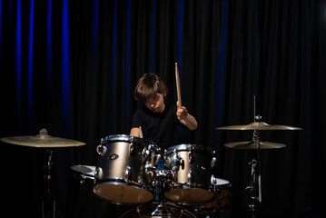 Fototapeta na wymiar The boy learns to play the drums in the studio on a black background. Music school student