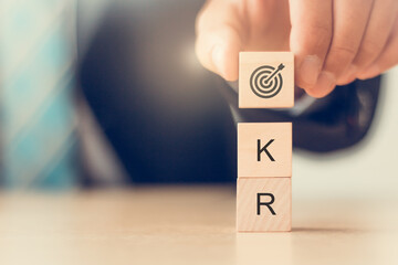 Business plan with OKR(Objectives and Key Results). Man holds wooden cube blocks with goal icon and OKR text. For developing business performance.  Achieve business growth by flexible management.
