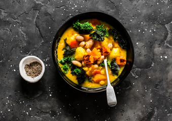 Vegetarian pumpkin, potatoes, beans and kale stew - delicious autumn lunch on a dark background, top view
