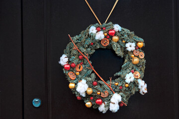 Christmas wreath decorated with fir branches, cones, and festive garland hanging on red wooden door. New year and winter holidays decoration. Holiday wreath on the door