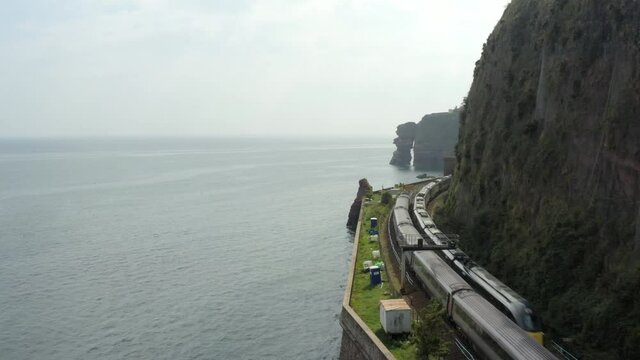 Two trains crossing over on the Devon coast with huge cliffs and sea rocks and beautiful views out to sea with a train entering a tunnel right on the coast near Dawlish