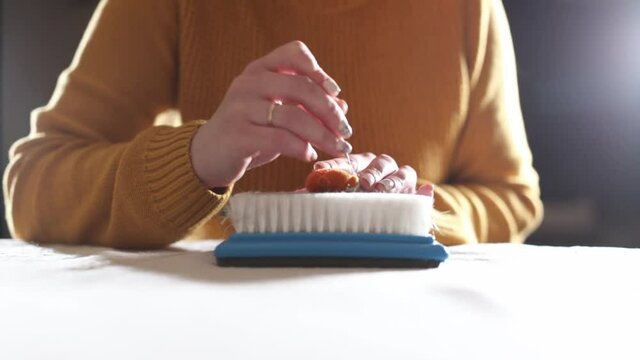 Dry felting, process. Woman girl in a yellow sweater rolls a brooch with a needle on a brush. Dark style. Handicraft and handmade concept