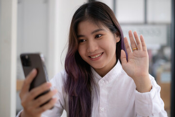 Portrait of Asian beautiful girl making video calling and waving hand for say hi by smartphone....