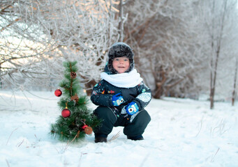 Children's portrait. Cute baby in a frosty winter park. A happy child is playing with snow and a Christmas tree on a snow walk. Christmas winter kids. Snow and snowflakes, frosty air, a child's smile