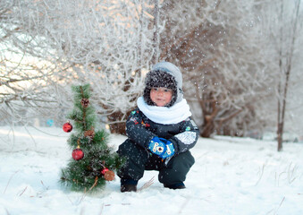 Children's portrait. Cute baby in a frosty winter park. A happy child is playing with snow and a Christmas tree on a snow walk. Christmas winter kids. Snow and snowflakes, frosty air, a child's smile