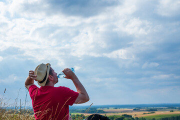 Traveler drinks water near the mountains.Hiker with backpack relaxing on top of the mountain in summer sunny day.