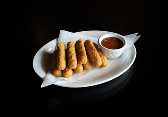 Closeup of mozzarella sticks with sauce on a plate isolated on a black background