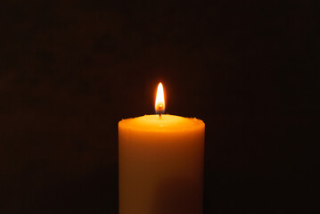One single light candle burning brightly in the black background.Spiritual candle yellow flame. Flame of candle in the darkness.Copy space.
