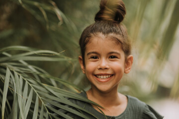 The face of a little girl surrounded by tropical leaves. Closeup portrait of a beautiful swarthy baby with perfect skin and dark hair. Natural cosmetics, health, cleanliness, skin care, beauty concept