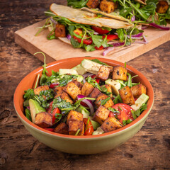 Vegetarian salad with vegetables, arugula, avocado and fried tofu in a bowl with vegan tacos in the...