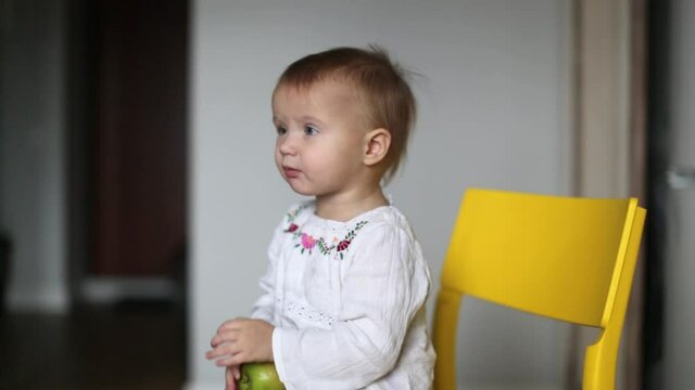 Cute caucasian child toddler eating green apple in kitchen in real interior