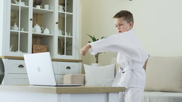 Little boy practicing karate techniques online in front of laptop at home