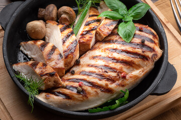 Roasted chicken fillet and mushrooms with herb in the frying pan on the wooden table close-up.