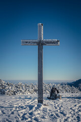 Mountain cross for hikers, Western Tatras, Poland. Tall wooden christian sign, snow on a peak, winter in the mountains. Selective focus on the structure, blurred background.