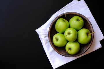 Green fresh apples in an old clay plate on a white cotton napkin on a black table. Modern stylish culinary template. Empty space for text or design.