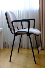 Stylish modern chair with a soft back and seat against a neutral beige room background. Simplicity and comfort.