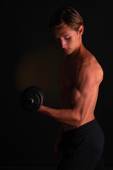 Fototapeta na wymiar Body profile of young athlete holding his dumbbell with his left arm during his biceps routine, studying his results, on black background. 