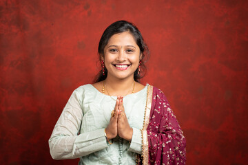 happy smiling Indian girl with traditional ethnic dress in namaste gesture looking at camera -...
