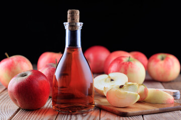 Bottle of apple cider and red apples on wooden background. Soft focus.