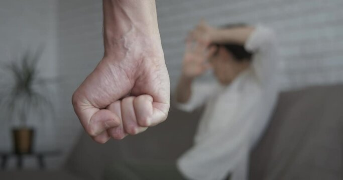 Male fist by female. A view of angry man fist by the scared woman sitting on the sofa.