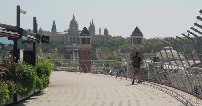 Man Walking At Terrace Of Arenas de Barcelona With Venetian Towers And Palau Nacional In Background In Barcelona, Spain. - wide shot