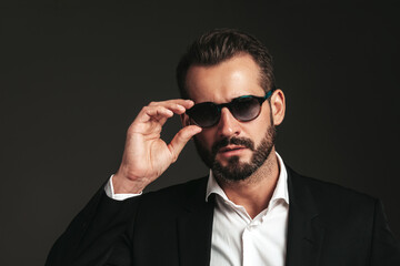 Obraz premium Closeup portrait of handsome confident stylish hipster lambersexual model. Sexy modern man dressed in elegant black suit. Fashion male posing in studio on dark background. In sunglasses